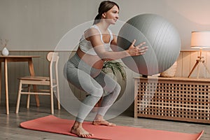 Pregnant woman exercising with fit ball at home, making squats with fitball.