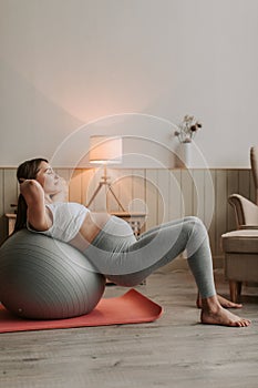 Pregnant woman exercising with fit ball at home, making squats with fitball.