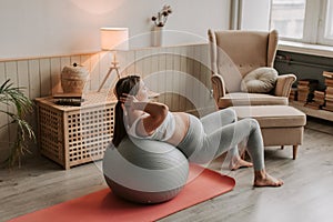 Pregnant woman exercising with fit ball at home, making squats with fitball.