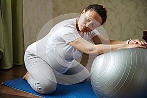 Pregnant woman exercising with fit ball, practicing pregnancy yoga, prenatal stretching and breathing exercises at home