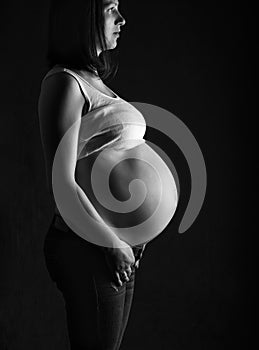 Pregnant woman, expectant mother on black background, monoshrome shoot.