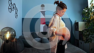 Pregnant woman expecting a baby caresses her belly standing in a living room
