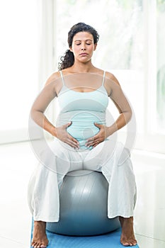 Pregnant woman with eyes closed touching her belly while sitting on ball