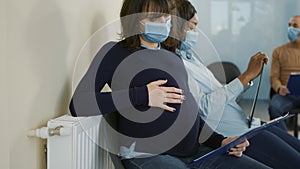 Pregnant woman with face mask sitting in waiting queue