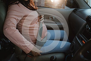 Pregnant woman fasten her seatbelt while sitting on a car