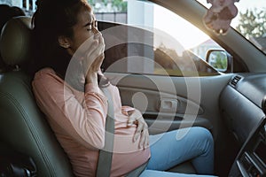 Pregnant woman fasten her seatbelt while sitting on a car