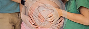 Pregnant Woman, father and first kid child holding hands in a heart shape on her baby bump. Pregnant Belly with fingers