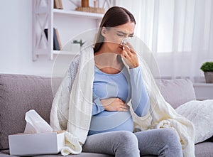 Pregnant Woman Feeling Unwell Blowing Nose Sitting On Couch Indoors