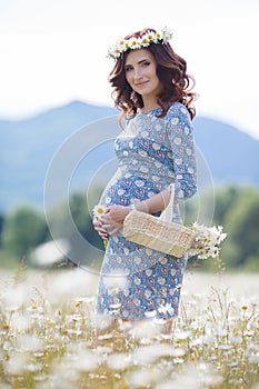 Pregnant woman in field with basket of white daisies