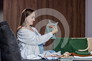 Pregnant woman folding baby clothes sitting on sofa at home