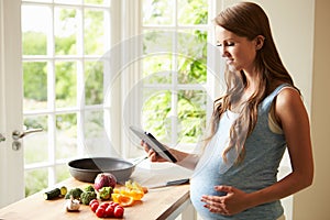 Pregnant Woman Following Recipe On Digital Tablet