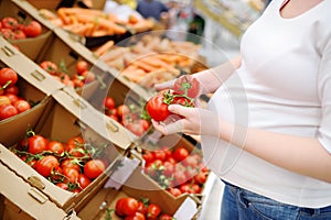 Pregnant woman in a food store or a supermarket choosing fresh organic tomatoes