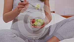 A pregnant woman with a fork eats vegetable salad, proper nutrition. A pregnant woman eats a vegetable salad useful for