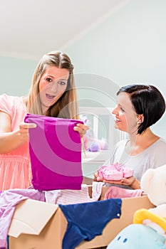 Pregnant woman and friend sharing baby clothes