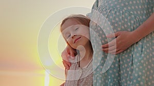 A pregnant woman gently hugs her daughter. Happy motherhood