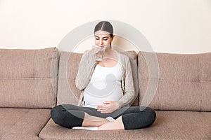 Pregnant woman with a glass of water sitting on sofa at the home