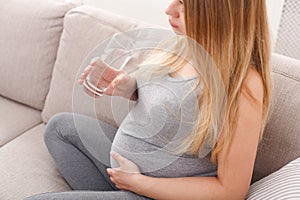 Pregnant woman with glass of water sitting on sofa