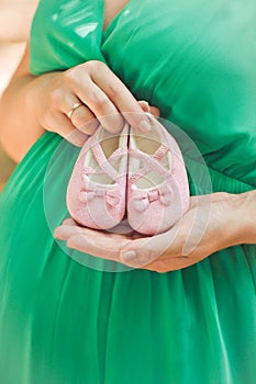 Pregnant woman in green dress belly holding pink baby booties, e