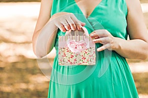 Pregnant woman in green dress pulls out a pink baby booties from