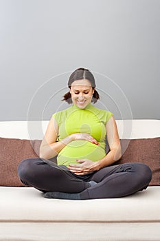 Pregnant woman in green t-shirt sitting on sofa