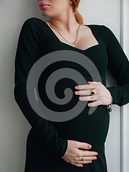 Pregnant woman with a hairstyle and makeup on her face in a black tight dress with white tulips