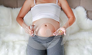 Pregnant woman hand with glass of water and fish oil tablets in hands