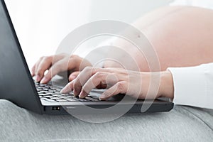 Pregnant women hand typing on keyboard on notebook to searching newborn baby . Using a laptop
