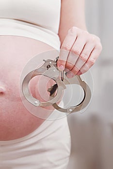 Pregnant woman with handcuffs on the background of her stomach, home living room