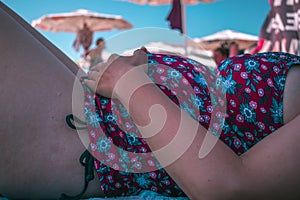 Pregnant woman with hands on her belly on the beach under umbrella protecting her self from the sun, pregnancy and sun avoid