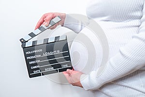 Pregnant woman hands holding clapper board on her belly. With Loading sign