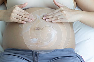 Pregnant woman hands lotion help skin belly on bedroom.