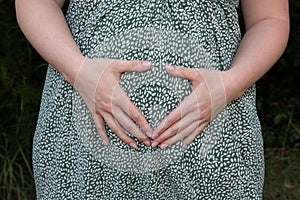 Pregnant woman hands make heart finger in belly