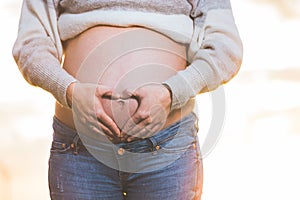 Pregnant woman hands making heart shape on belly.