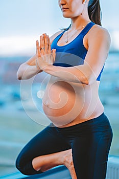 Pregnant woman with hands in namaste gesture stand in tree pose