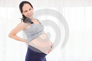 Pregnant woman having backache standing over bright window
