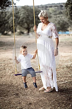 Pregnant woman having fun with her toddler son on the swing