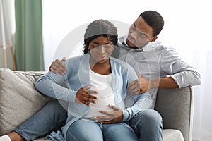 Pregnant woman having labor pains, sitting by husband on couch