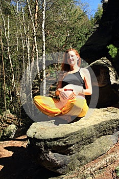 Pregnant woman with heart on belly sitting on stone