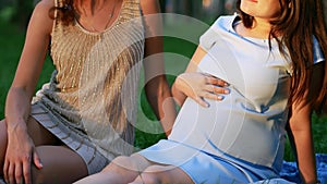 Pregnant woman and her friend sitting on grass