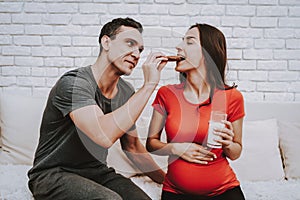 A pregnant woman and her husband eat together cookies.