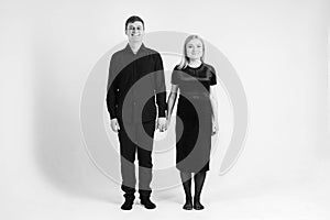 Pregnant woman and her husband holding hands in black clothes on a white background. Black and white picture. Beautiful married