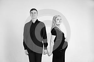 Pregnant woman and her husband holding hands in black clothes on a white background. Black and white picture. Beautiful married