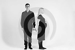 Pregnant woman and her husband holding hands in black clothes on a white background. Black and white picture. Beautiful married