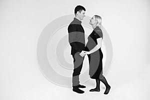 Pregnant woman and her husband holding hands in black clothes on a white background. Black and white picture. Beautiful married