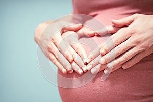 Pregnant Woman and her husband holding hands in a heart shape on her baby bump. Pregnant Belly with fingers Heart symbol