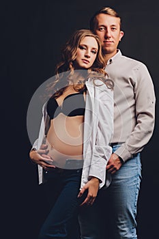 pregnant woman her husband holding her tummy.Beautiful belly of young attractive pregnant woman over black background.