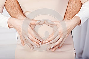 Pregnant woman and her husband holding making heart shape with hands on pregnant belly