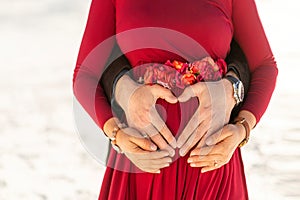 Pregnant woman and her husband hug and make hearts with their hands