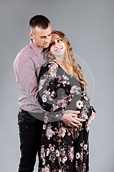 A pregnant woman and her husband are hugging on a gray background in the studio