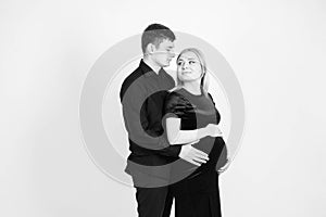 Pregnant woman and her husband hugging and holding onto your stomach in black clothes on a white background. Black and white